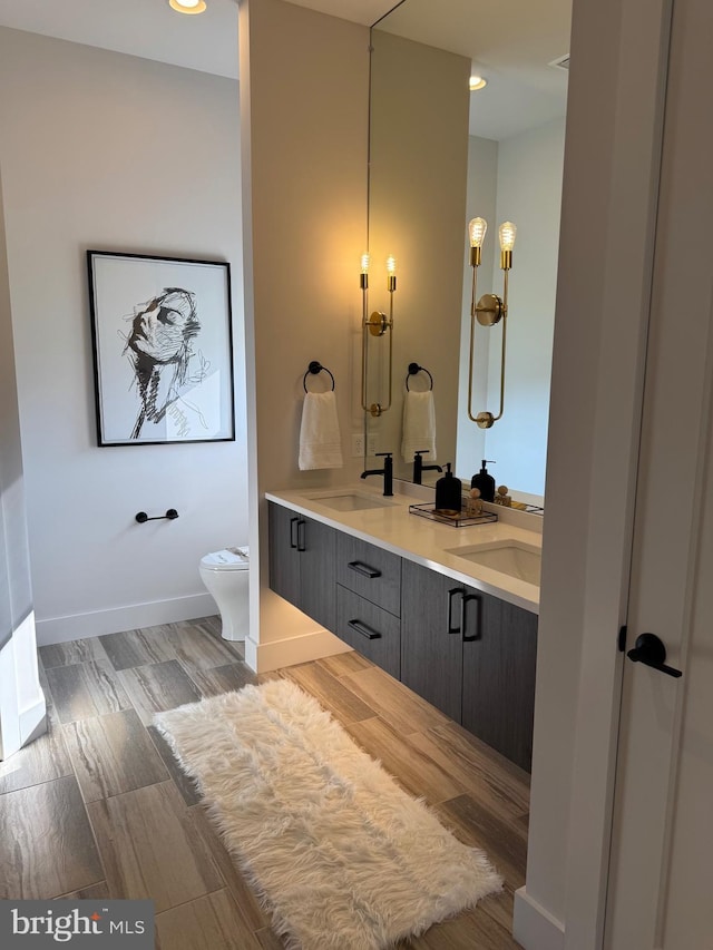 bathroom with toilet, double vanity, baseboards, and a sink