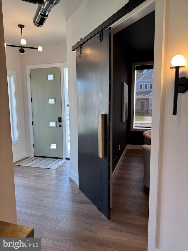 hall with a barn door, wood finished floors, and baseboards