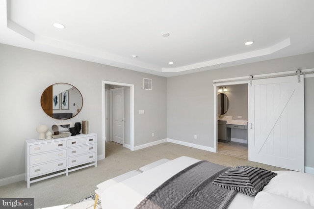 carpeted bedroom featuring a barn door, ensuite bathroom, and a tray ceiling