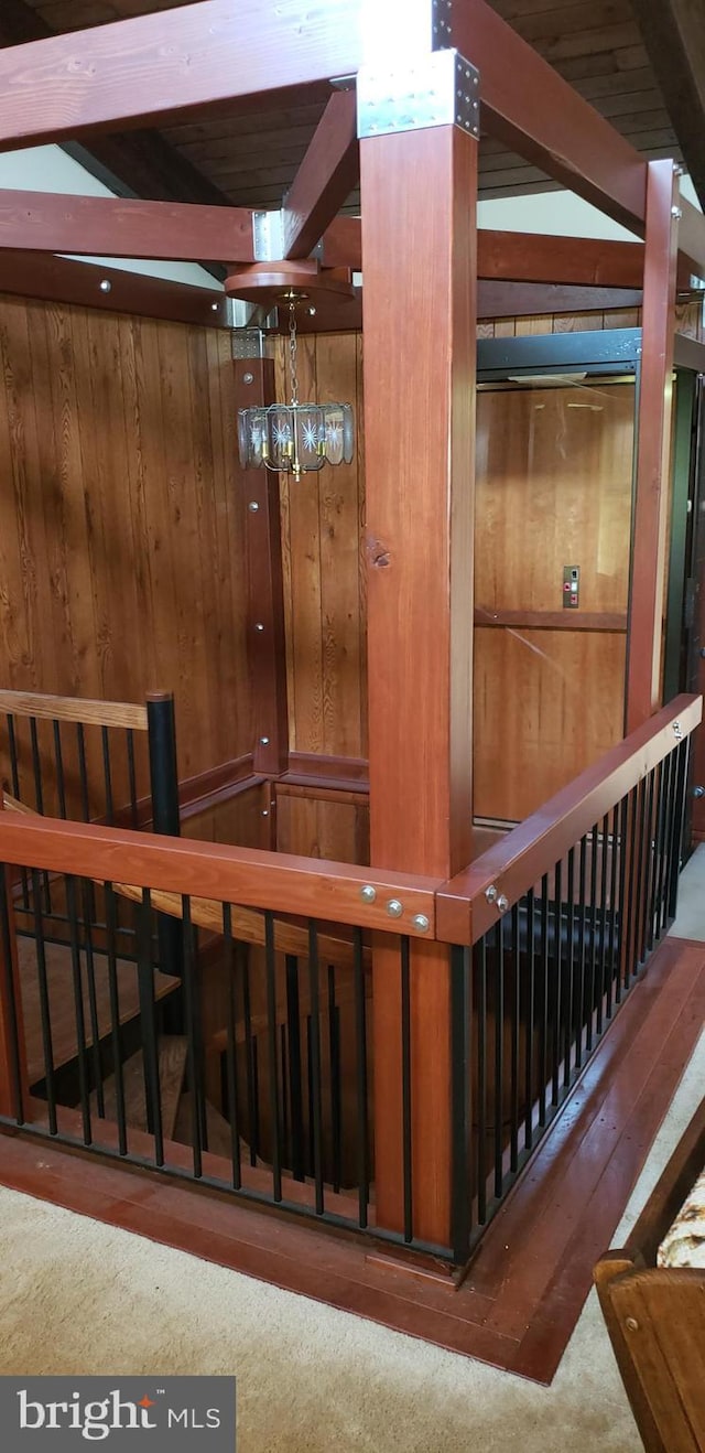 stairway with a chandelier, wood walls, dark colored carpet, and beamed ceiling