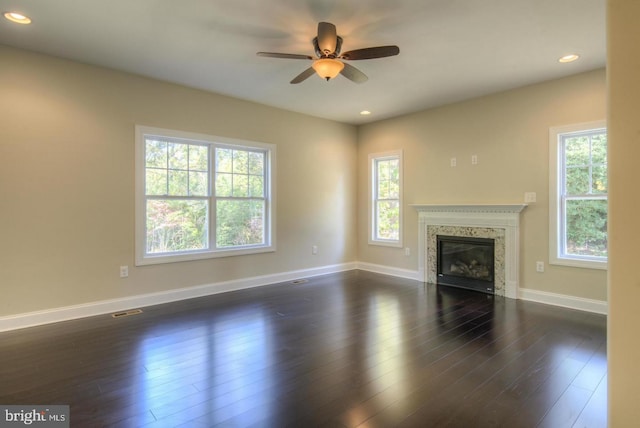 unfurnished living room with a fireplace, ceiling fan, dark wood-type flooring, and a wealth of natural light