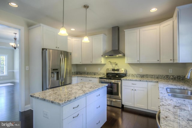 kitchen featuring wall chimney range hood, dark wood-type flooring, stainless steel appliances, decorative light fixtures, and white cabinets