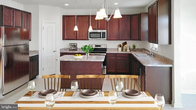 kitchen with sink, light stone counters, a kitchen island, stainless steel appliances, and decorative light fixtures