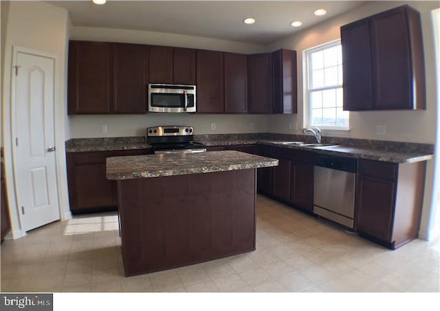 kitchen with sink, dark stone counters, appliances with stainless steel finishes, light tile flooring, and a center island