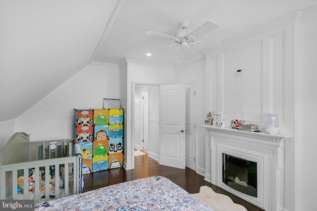 bedroom with ceiling fan, vaulted ceiling, a nursery area, dark hardwood / wood-style flooring, and ornamental molding