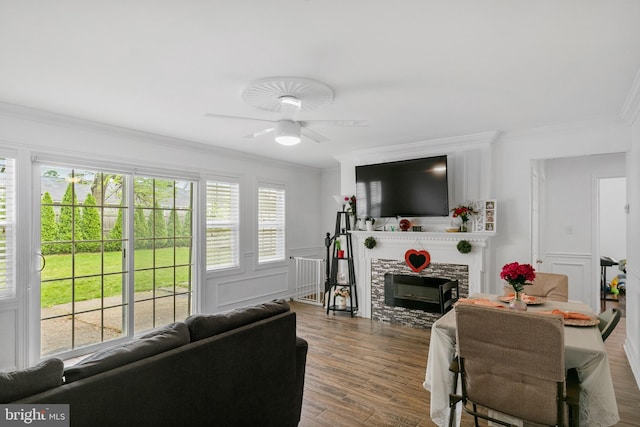 living room featuring ceiling fan, dark wood-type flooring, ornamental molding, and a stone fireplace