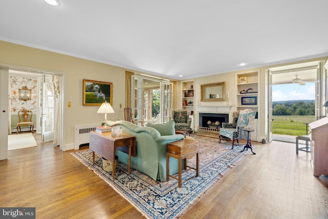 living room featuring a baseboard heating unit, ornamental molding, radiator, built in features, and light wood-type flooring