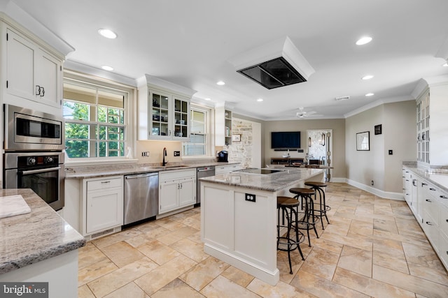 kitchen with ceiling fan, stainless steel appliances, white cabinetry, and an island with sink