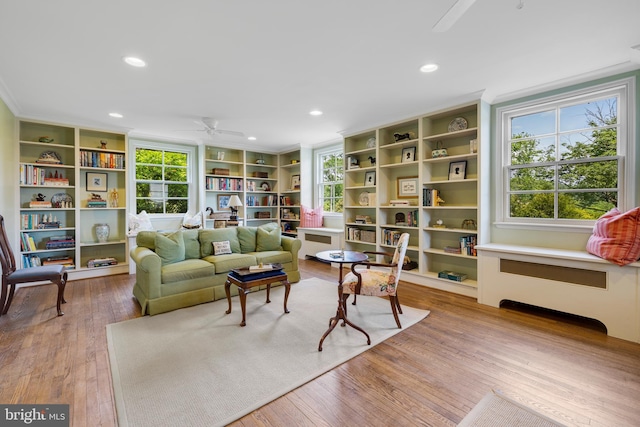 living room featuring ceiling fan, light wood-type flooring, built in features, crown molding, and radiator heating unit