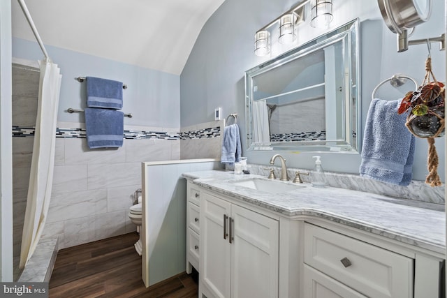 bathroom with toilet, large vanity, vaulted ceiling, wood-type flooring, and tile walls