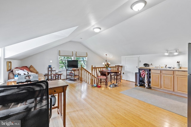 living room with a notable chandelier, vaulted ceiling with skylight, and light hardwood / wood-style flooring