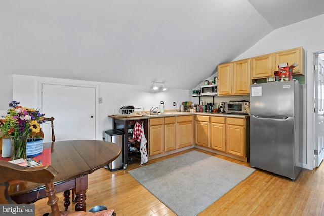 kitchen featuring light brown cabinets, lofted ceiling, stainless steel fridge, and light wood-type flooring