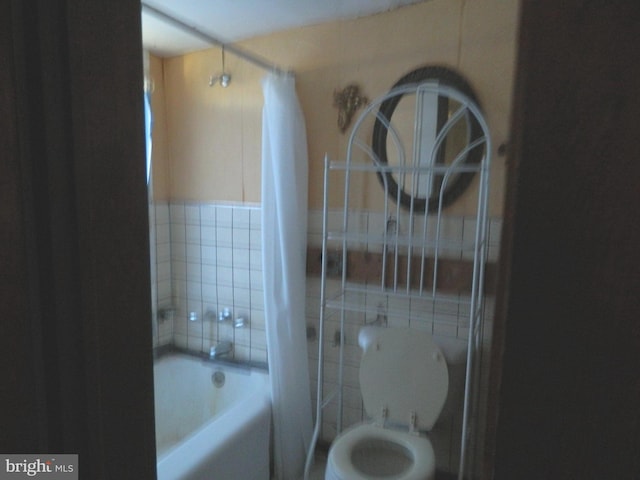 bathroom featuring toilet, shower / bath combo with shower curtain, and tile walls