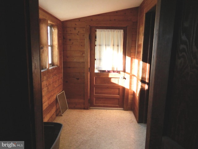 entryway featuring light colored carpet, wooden walls, and vaulted ceiling