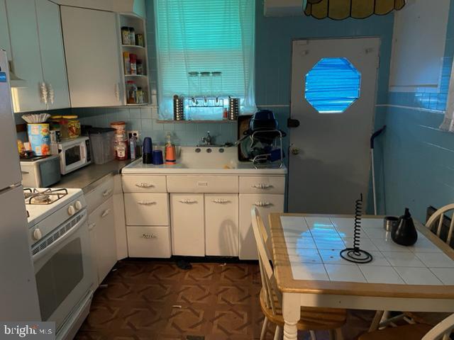 kitchen with backsplash, tile counters, white appliances, and white cabinetry