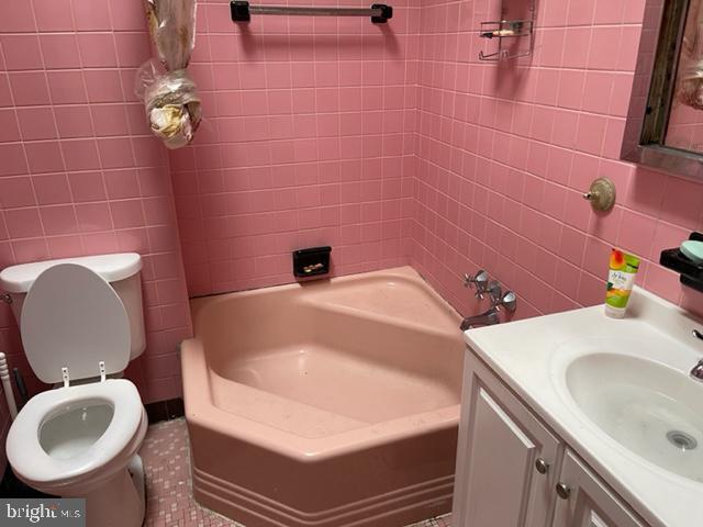 full bathroom with toilet, large vanity, tiled shower / bath combo, tile walls, and tile floors