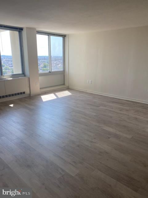 spare room featuring a baseboard heating unit and dark hardwood / wood-style flooring