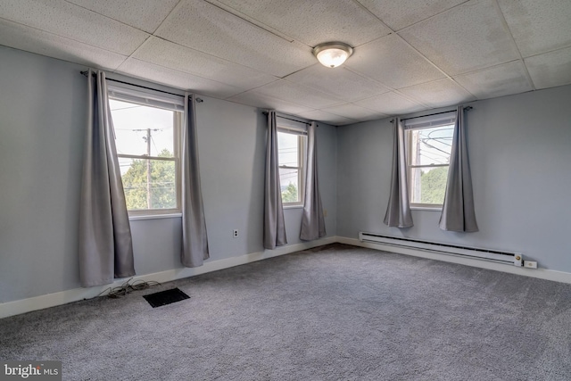 carpeted empty room with a drop ceiling, a baseboard heating unit, and a healthy amount of sunlight