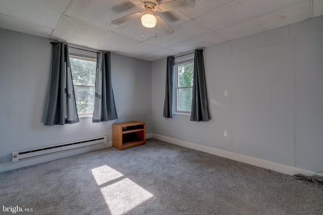 unfurnished room featuring plenty of natural light, baseboard heating, ceiling fan, and a drop ceiling