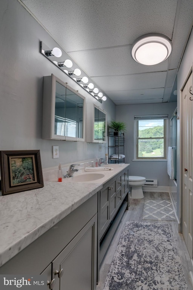 bathroom featuring baseboard heating, a drop ceiling, wood-type flooring, toilet, and vanity