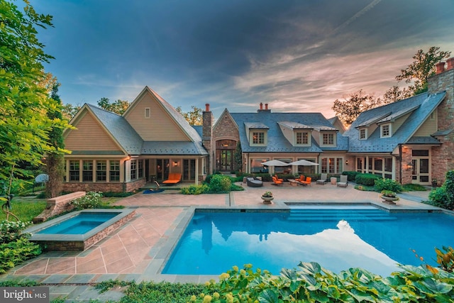 back house at dusk with a patio area and a swimming pool with hot tub