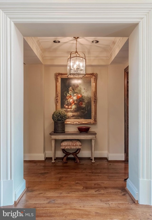 hallway featuring a raised ceiling, hardwood / wood-style flooring, and an inviting chandelier