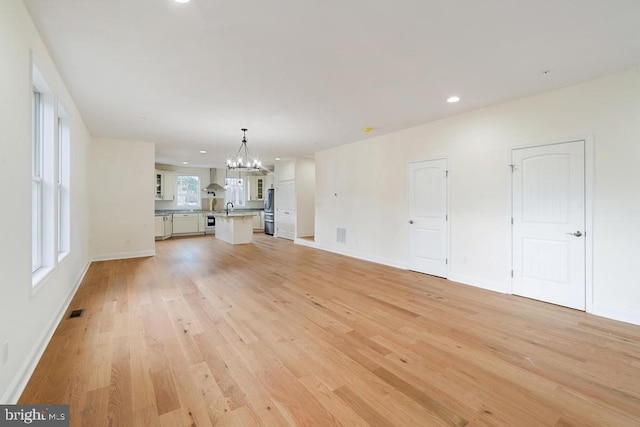 unfurnished living room with light hardwood / wood-style flooring, a chandelier, and sink