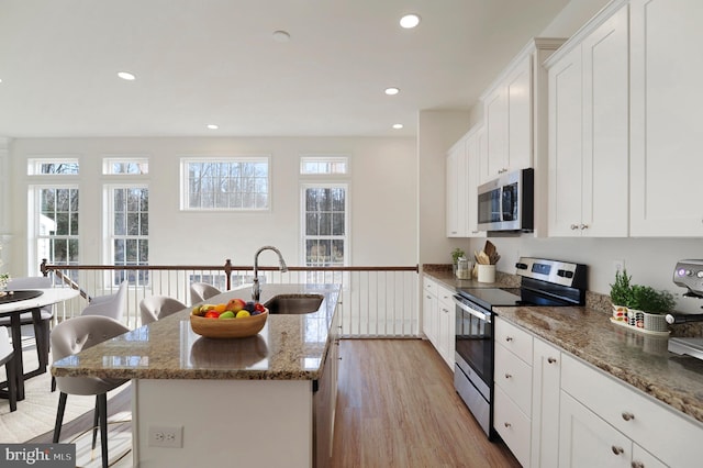 kitchen featuring sink, white cabinets, appliances with stainless steel finishes, a center island with sink, and light wood-type flooring