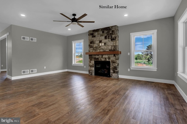 unfurnished living room featuring ceiling fan, a stone fireplace, dark wood-type flooring, and a wealth of natural light