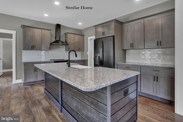 kitchen featuring stainless steel fridge with ice dispenser, wall chimney exhaust hood, dark hardwood / wood-style flooring, and an island with sink