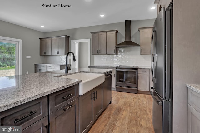 kitchen featuring stainless steel appliances, wall chimney exhaust hood, sink, light wood-type flooring, and light stone counters