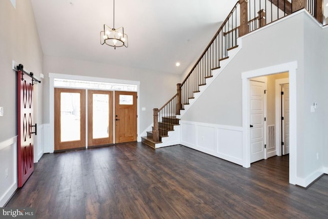 foyer with a barn door, dark hardwood / wood-style floors, a chandelier, and a towering ceiling