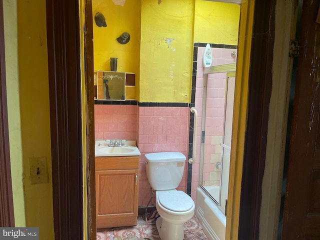 full bathroom with vanity, tile walls, tile floors, bath / shower combo with glass door, and toilet