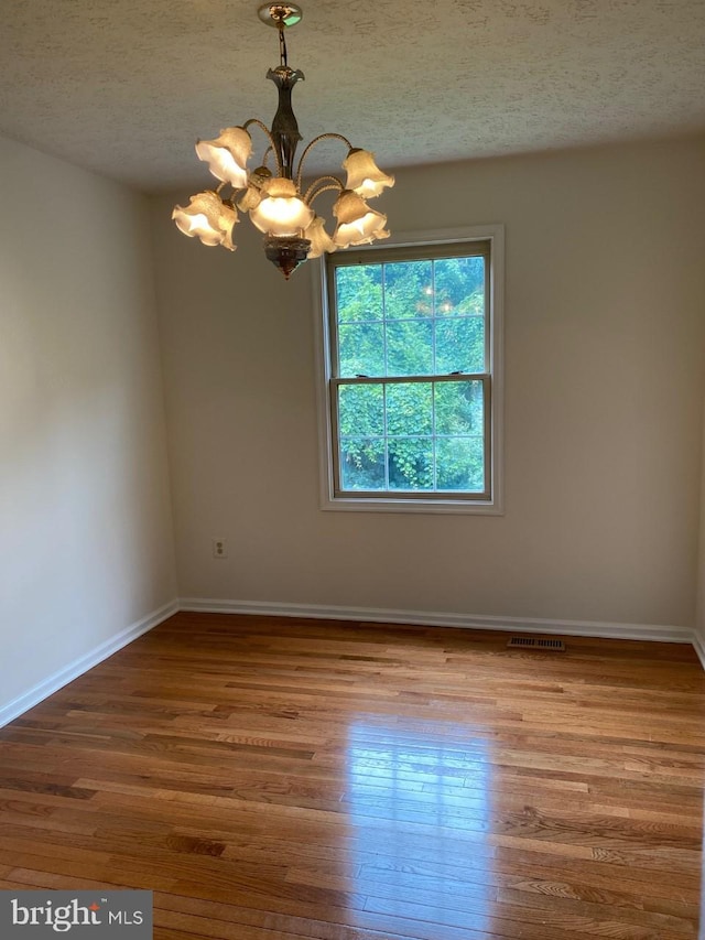 empty room with hardwood / wood-style floors, a textured ceiling, and a notable chandelier