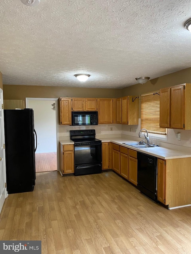 kitchen featuring sink, black appliances, a textured ceiling, and light hardwood / wood-style floors