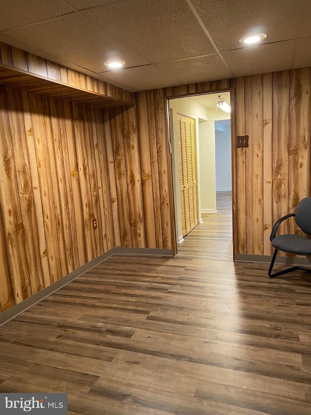 interior space with hardwood / wood-style floors, a drop ceiling, and wood walls