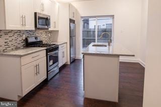 kitchen with tasteful backsplash, appliances with stainless steel finishes, white cabinets, a kitchen island with sink, and dark hardwood / wood-style floors