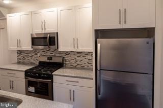 kitchen with backsplash, stainless steel appliances, and white cabinetry