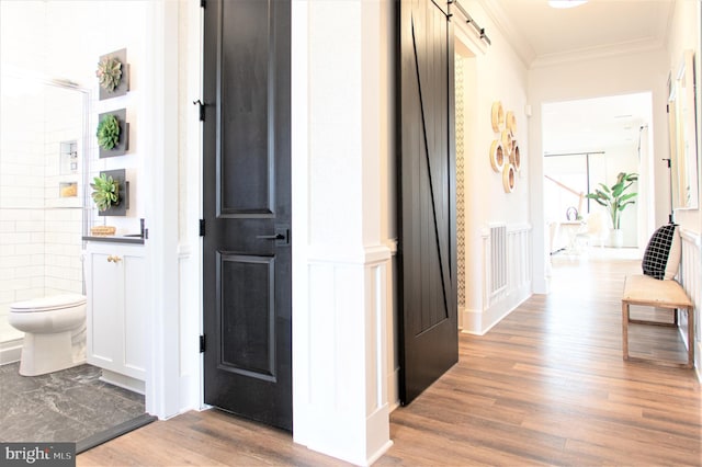 corridor featuring tile walls, ornamental molding, a barn door, and hardwood / wood-style flooring