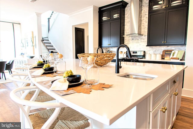 kitchen featuring an island with sink, tasteful backsplash, hardwood / wood-style floors, wall chimney exhaust hood, and crown molding