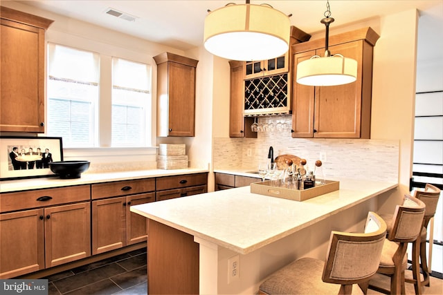 kitchen with decorative light fixtures, tasteful backsplash, kitchen peninsula, dark tile flooring, and a kitchen breakfast bar