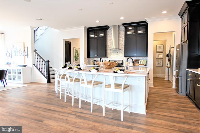 kitchen featuring wall chimney exhaust hood, tasteful backsplash, wood-type flooring, and a kitchen breakfast bar