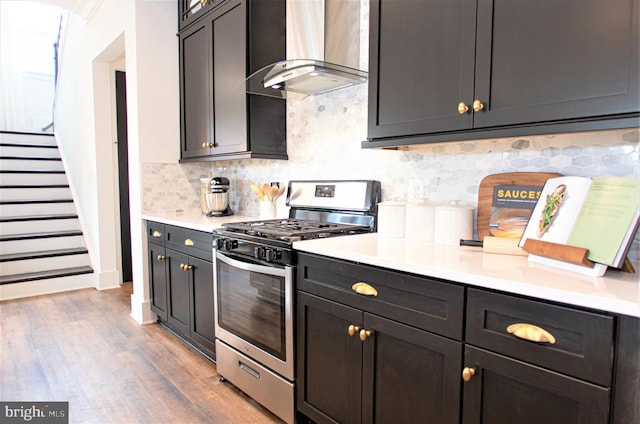 kitchen featuring wood-type flooring, tasteful backsplash, wall chimney exhaust hood, and stainless steel gas range oven