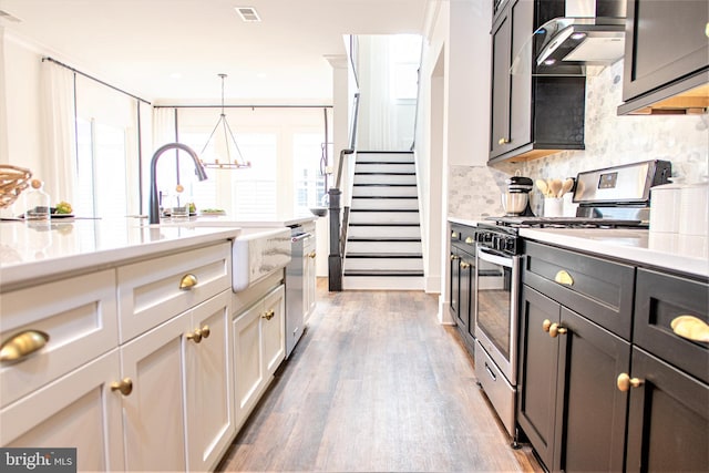 kitchen with tasteful backsplash, wood-type flooring, stainless steel appliances, decorative light fixtures, and wall chimney exhaust hood