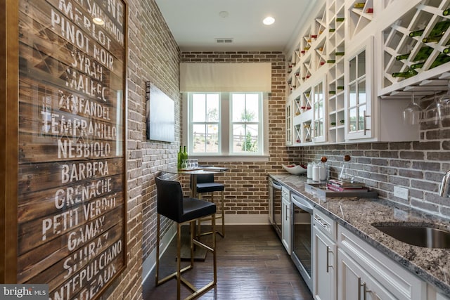 kitchen featuring wine cooler, sink, brick wall, white cabinetry, and light stone countertops