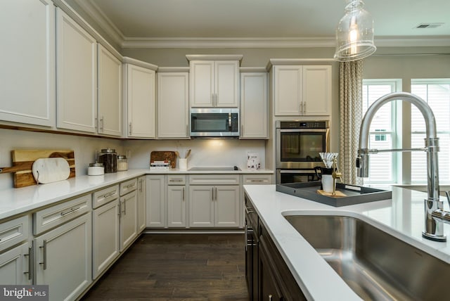 kitchen featuring hanging light fixtures, dark wood-type flooring, stainless steel appliances, sink, and ornamental molding