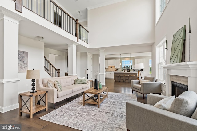 living room featuring crown molding, decorative columns, a towering ceiling, and dark hardwood / wood-style flooring