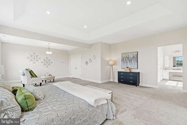 bedroom featuring light carpet, ensuite bath, and a tray ceiling