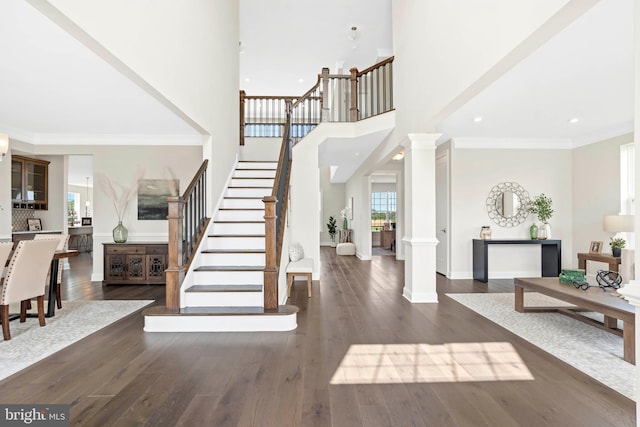 entrance foyer featuring crown molding, decorative columns, and dark wood-type flooring