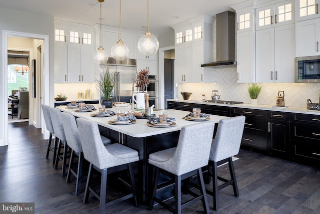 kitchen featuring wall chimney exhaust hood, white cabinets, a center island with sink, and stainless steel appliances